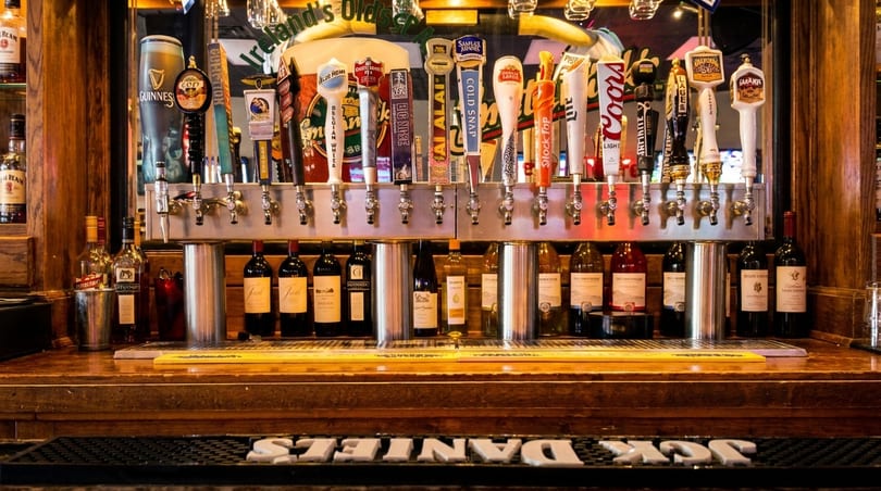 A bar with many beer taps, bottles of wine, and liquor on wooden shelves.