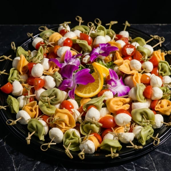 Colorful tortellini, cherry tomatoes, and mozzarella balls on skewers, garnished with orchids and orange slices.