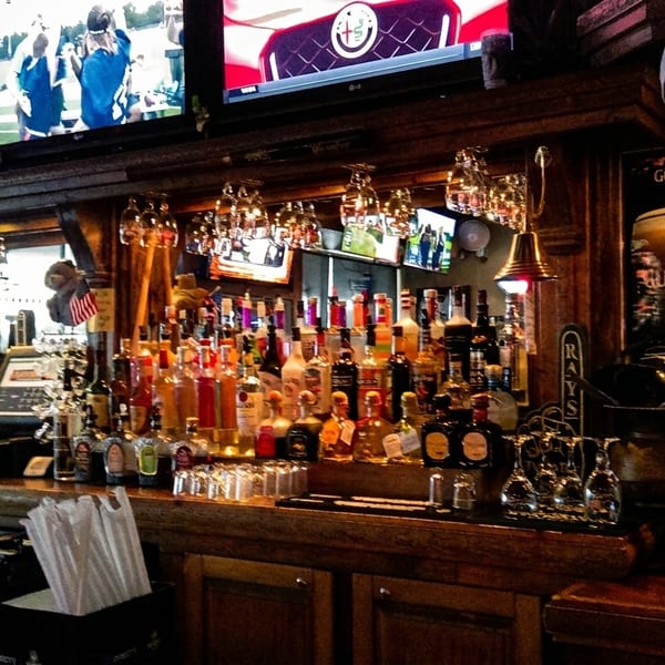 A well-stocked bar with numerous liquor bottles, beer taps, and TVs showing sports.