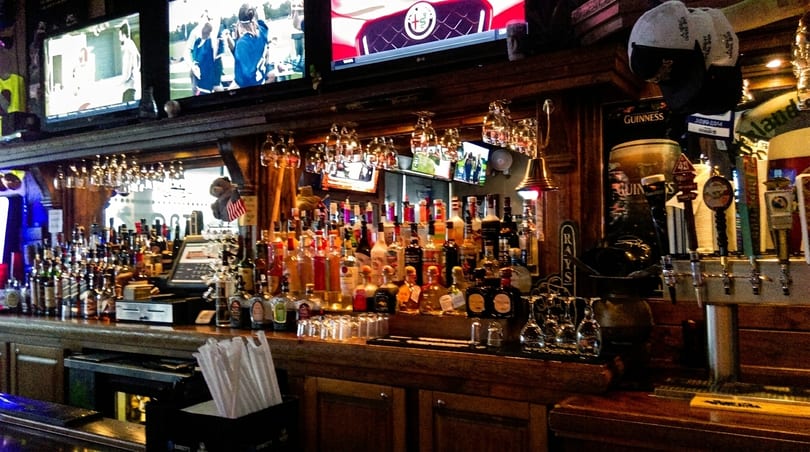 A well-stocked bar with numerous liquor bottles, beer taps, and TVs showing sports.