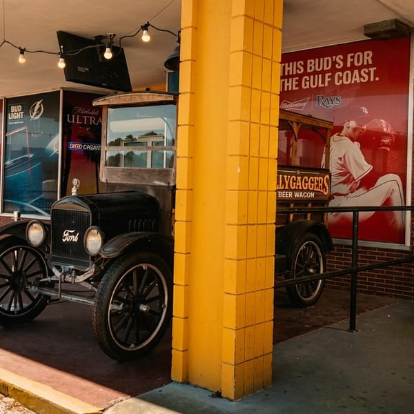 Vintage black Ford truck parked outside a restaurant with yellow pillars and beer advertisements.