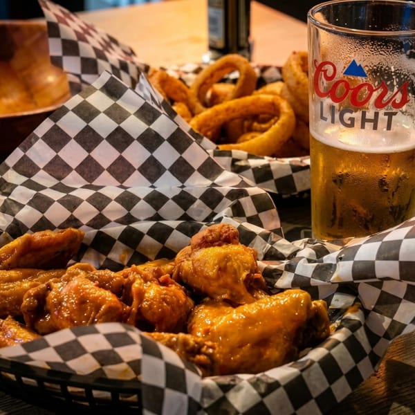Basket of chicken wings and onion rings with a glass of Coors Light beer.