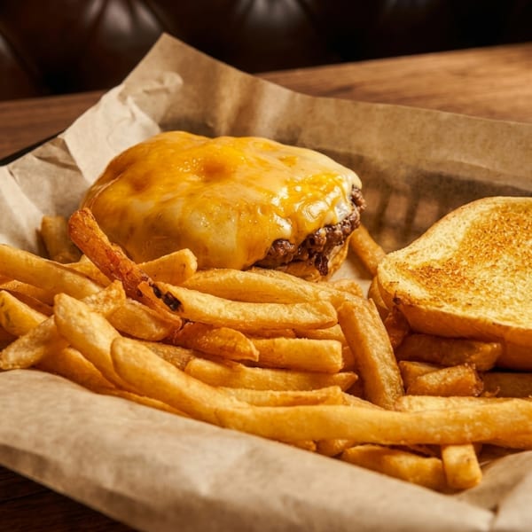 Cheeseburger with melted cheese and a side of golden french fries in a basket.