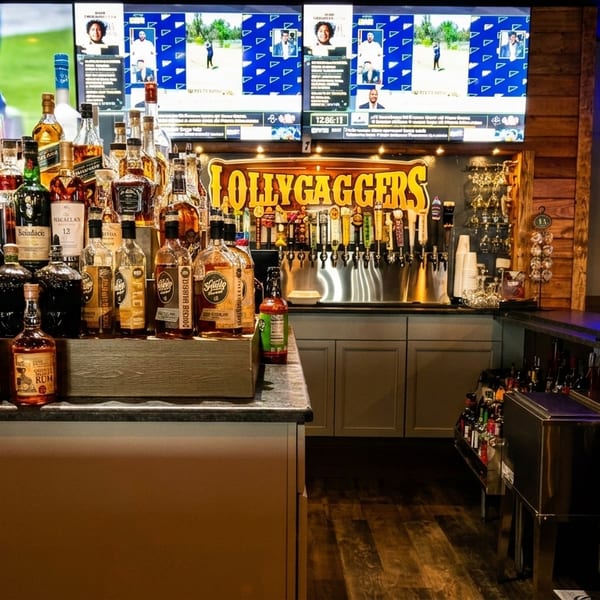 A well-stocked bar at Lollygaggers with liquor bottles, beer taps, and sports on multiple TVs.