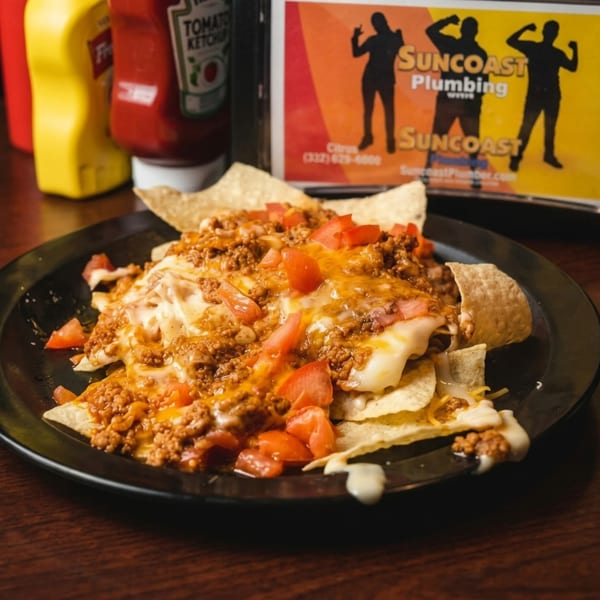 A plate of nachos with melted cheese, ground beef, and diced tomatoes on a wooden table.