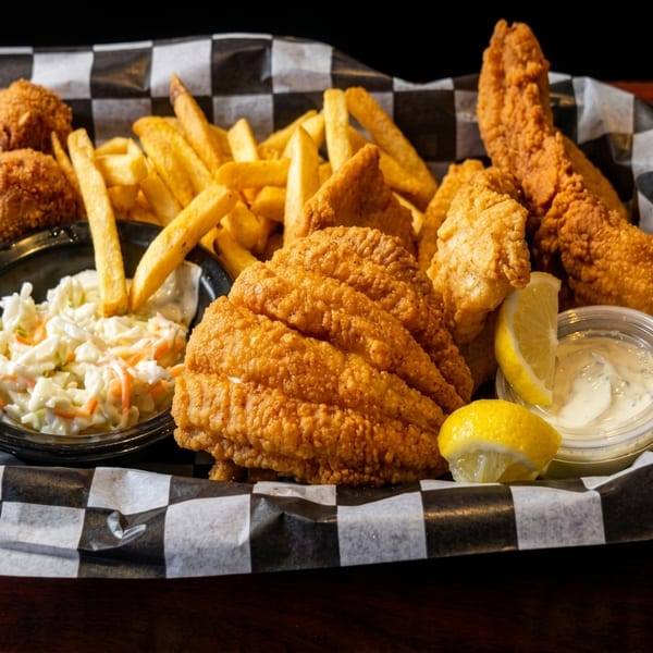 Fried fish and hush puppies with french fries, coleslaw, lemon, and tartar sauce in a basket.