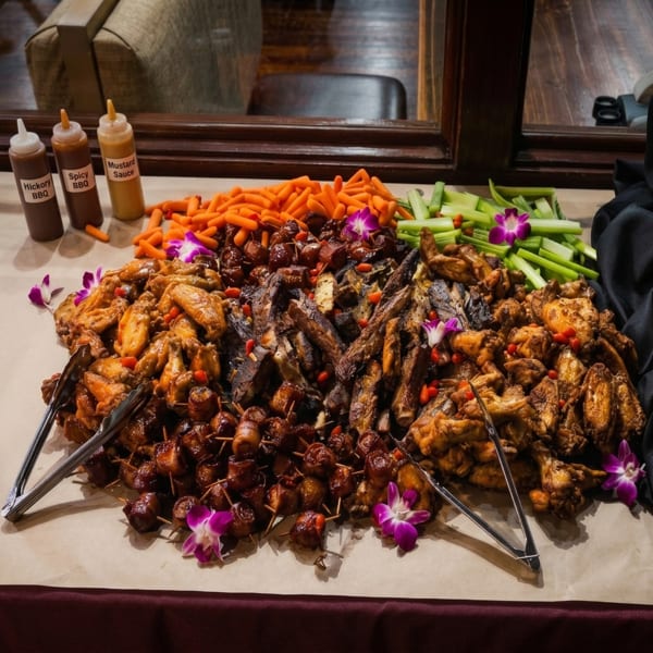 A buffet spread with BBQ ribs, chicken wings, bacon-wrapped bites, carrots, and celery.
